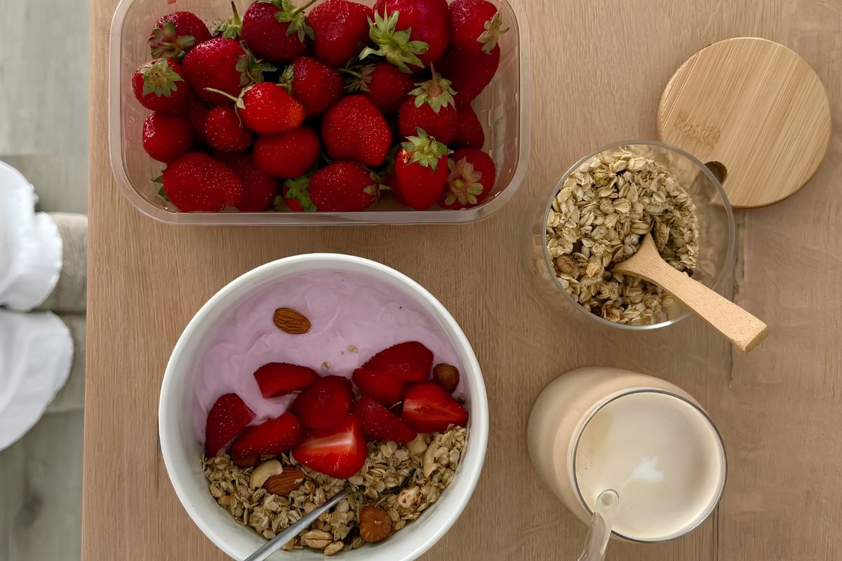 Woman holding a pink bowl filled with fresh strawberries and granola, with an iced matcha latte and basket of strawberries in the background