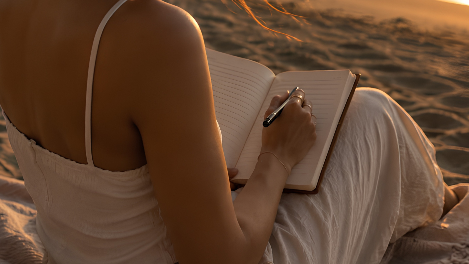woman journaling on the beach at sunset - june journal prompts by zodiac sign